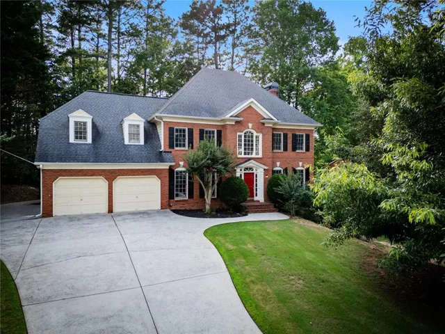 Brick exterior featuring a two-story design, attached two-car garage, dormer windows, and a prominent front entrance with a red door