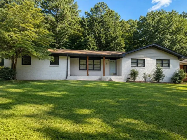 Exterior featuring white painted brick, a covered porch with natural wood columns, black window trim, and a gabled roofline