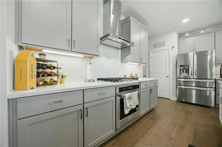 Kitchen featuring light gray cabinetry, stainless steel appliances, a gas range with an overhead vent hood, white subway tile backsplash, and light wood-finish flooring