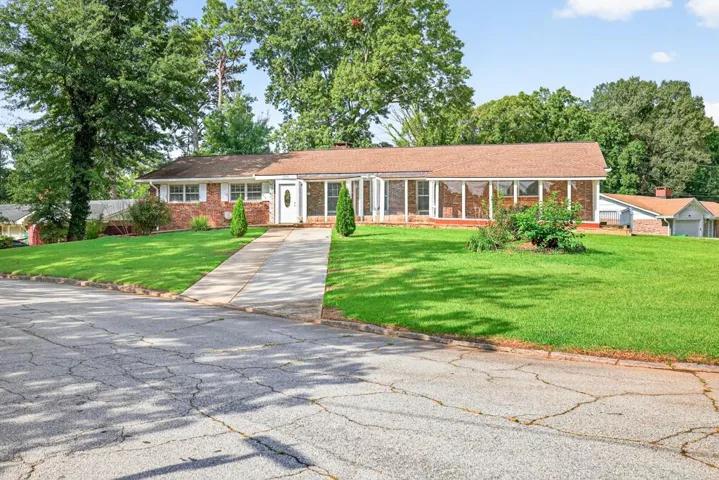 Brick exterior with white trim, screened-in porch, mature trees, and a concrete driveway