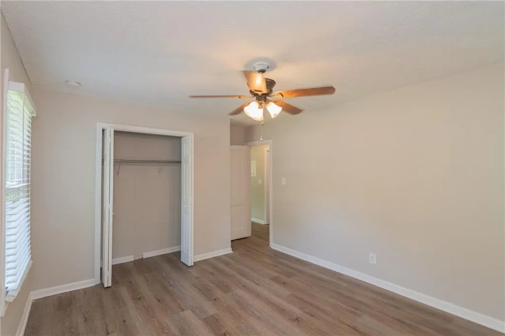 Unfurnished bedroom featuring wood finished floors, a closet, baseboards, and ceiling fan
