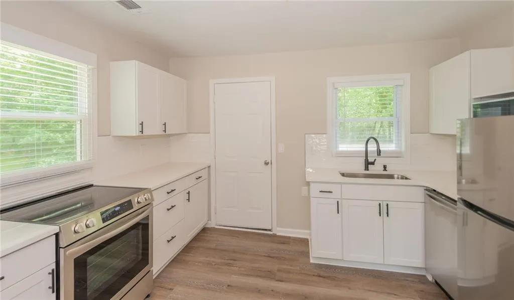 Kitchen with appliances with stainless steel finishes, a sink, light wood finished floors, white cabinetry, and decorative backsplash