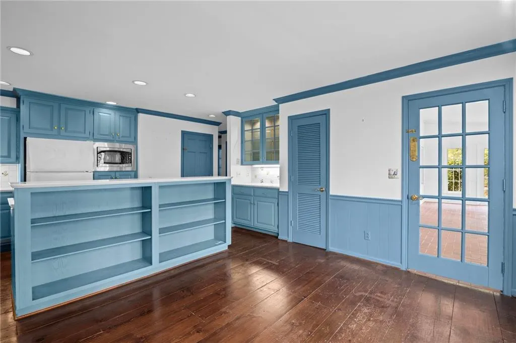 Kitchen with blue cabinets, light countertops, open shelves, dark wood-style floors, and wainscoting