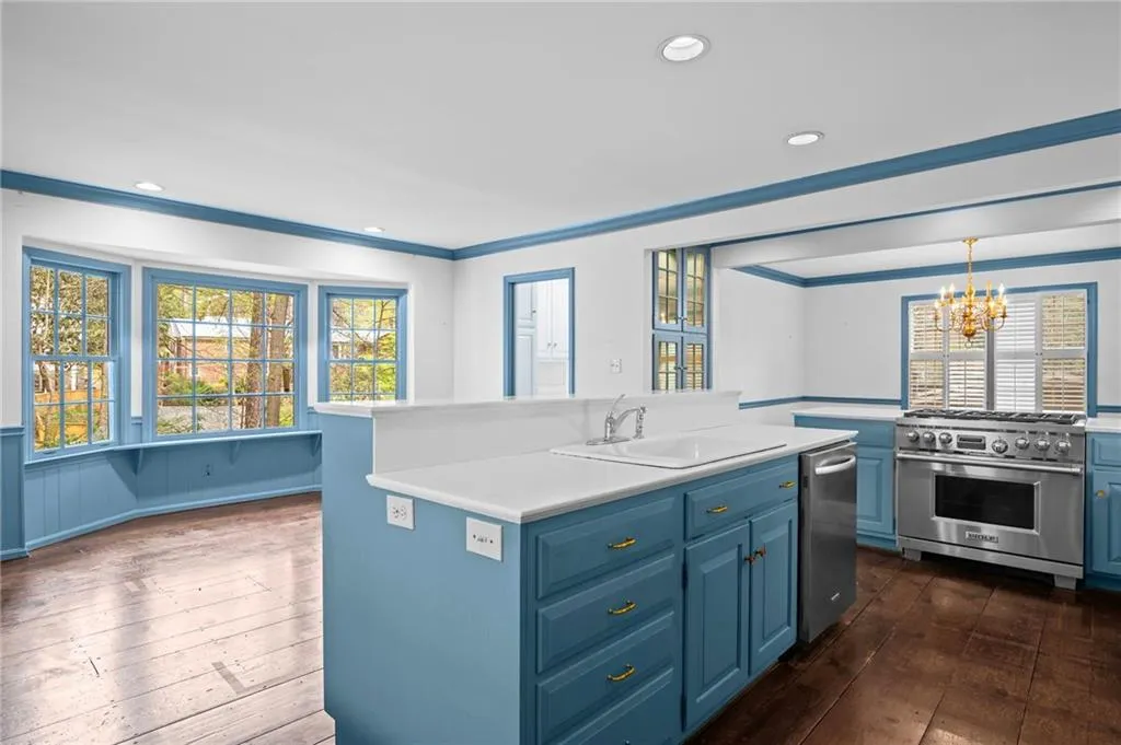 Kitchen with blue cabinetry, dark wood-style flooring, stainless steel appliances, a center island with sink, and light countertops