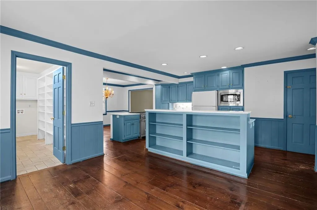 Kitchen with blue cabinets, wainscoting, a kitchen island, light countertops, and hanging lights
