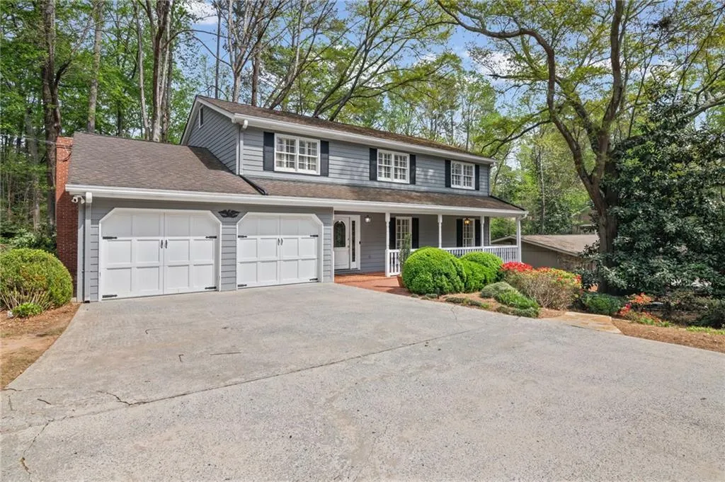 Traditional-style home with a porch, driveway, an attached garage, a chimney, and roof with shingles