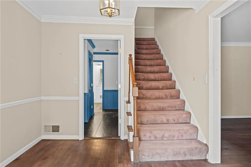 Stairway with ornamental molding, hardwood / wood-style floors, and hanging lights