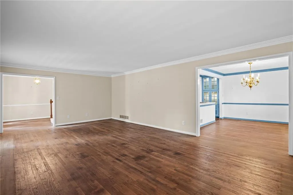 Empty room with suspended lighting, dark wood-style floors, and ornamental molding
