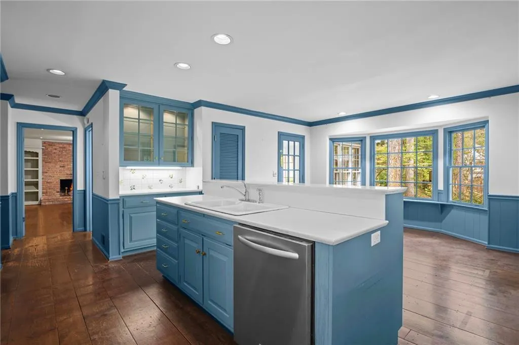 Kitchen featuring a wainscoted wall, blue cabinets, dishwasher, light countertops, and glass insert cabinets