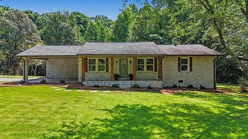 Charming single-story residence featuring a brick and stone exterior with a covered front porch, multiple large windows with wood-finish frames, and a welcoming green entry door