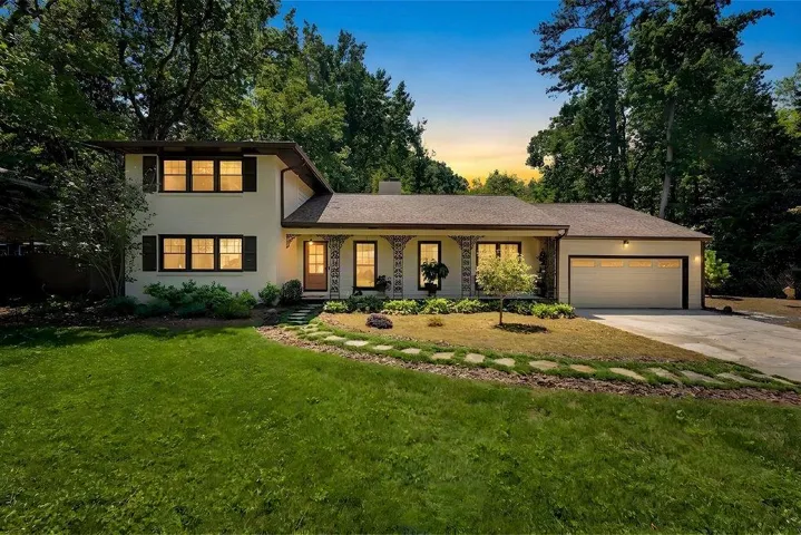 White exterior with dark shutters, covered front porch, attached garage, and stone paver pathway