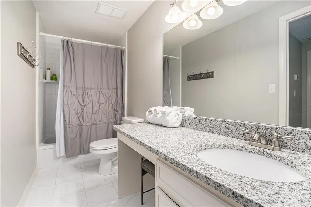 Bathroom with marble finish floors, toilet, vanity, and curtained shower