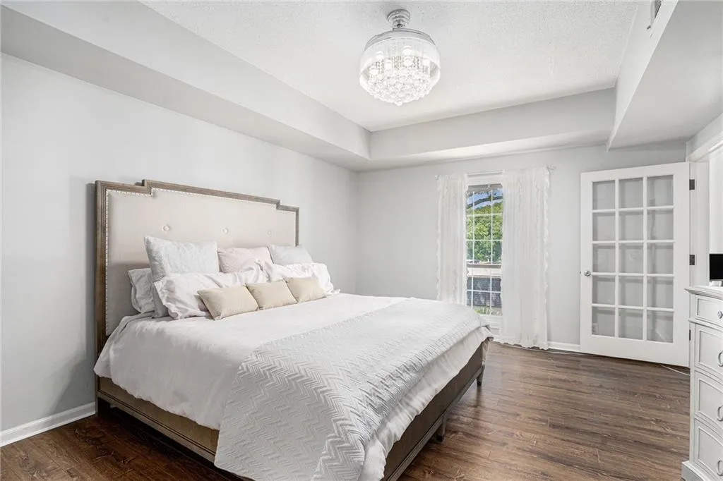 Bedroom with dark wood-type flooring, baseboards, a chandelier, and a tray ceiling