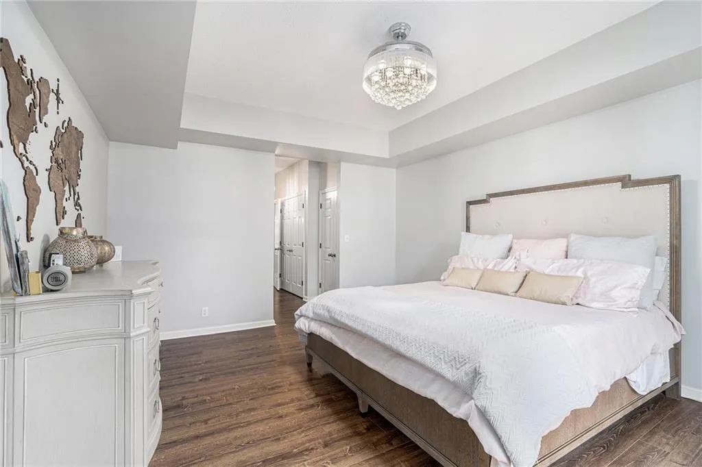 Bedroom with dark wood-style floors, baseboards, a chandelier, and a tray ceiling