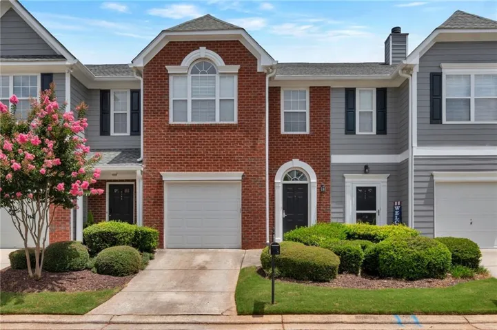 Brick and siding exterior featuring an arched window, white garage door, and mature landscaping