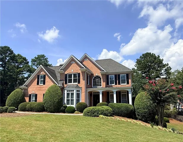 Brick Colonial estate showcasing a symmetrical façade with arched entryway, multi-pane windows with black shutters, and a steeply pitched roofline