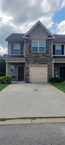 Stone veneer facade, attached garage, concrete driveway, front entry door, and exterior wall sconces