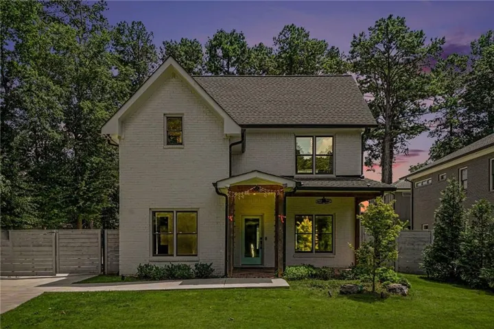 Two-story residence featuring white brick exterior, dark-framed windows, a covered front porch with wood-look columns, and a dark-shingled roof