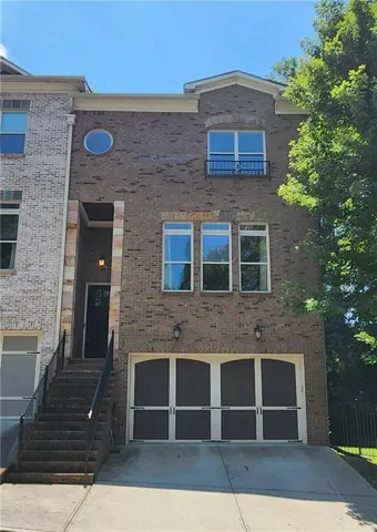 Three story brick townhome exterior featuring an arched garage door, prominent entryway stairs with wrought iron railings, a stone-accented front porch, and upper-level windows including a circular accent window