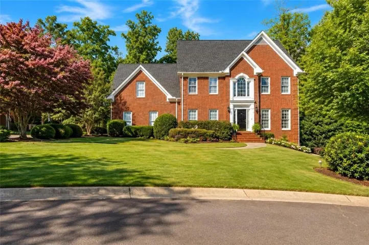 Brick exterior with white trim, arched dormer window, and an expansive lawn with established landscaping