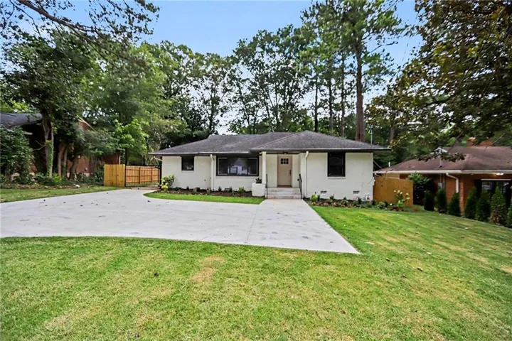 Single-story white exterior residence featuring a dark roof, a front door with a small square window, a concrete driveway, and a front lawn