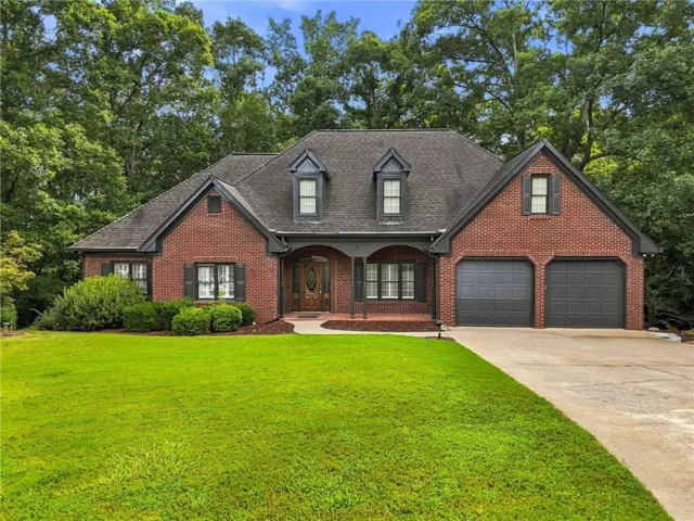 Brick exterior with dark gray trim, covered front entry, two dormer windows, and a two-car garage