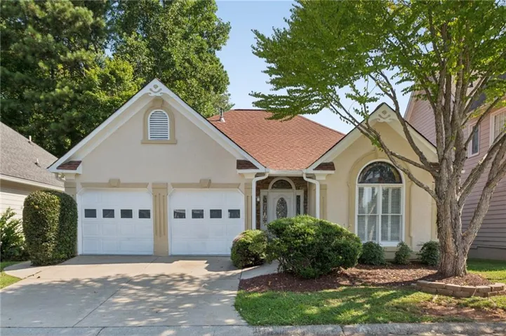 Stucco exterior with a two-car garage, arched window, and landscaped front yard with mature trees
