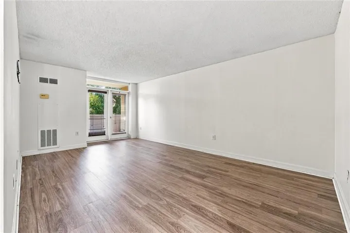 Wood-finish flooring throughout, white painted walls, and double glass doors opening to an exterior balcony