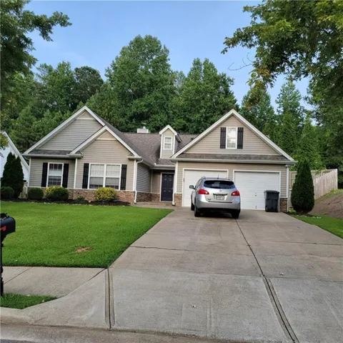 Ranch-style residence featuring a two-car garage, dormer window, stone accent siding, dark shutters, and a concrete driveway