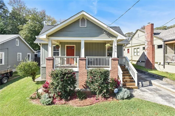 Green siding home featuring a covered front porch with white railings, a contrasting red front door, and brick column bases