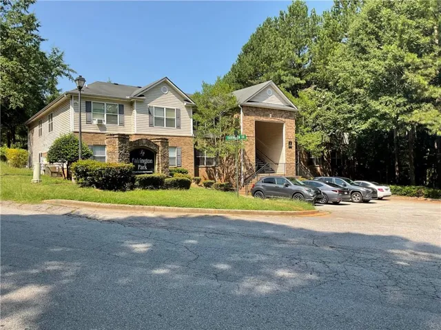 Two-story building exterior with stone and siding facade, featuring a prominent entrance archway, dedicated parking area, and mature landscaping