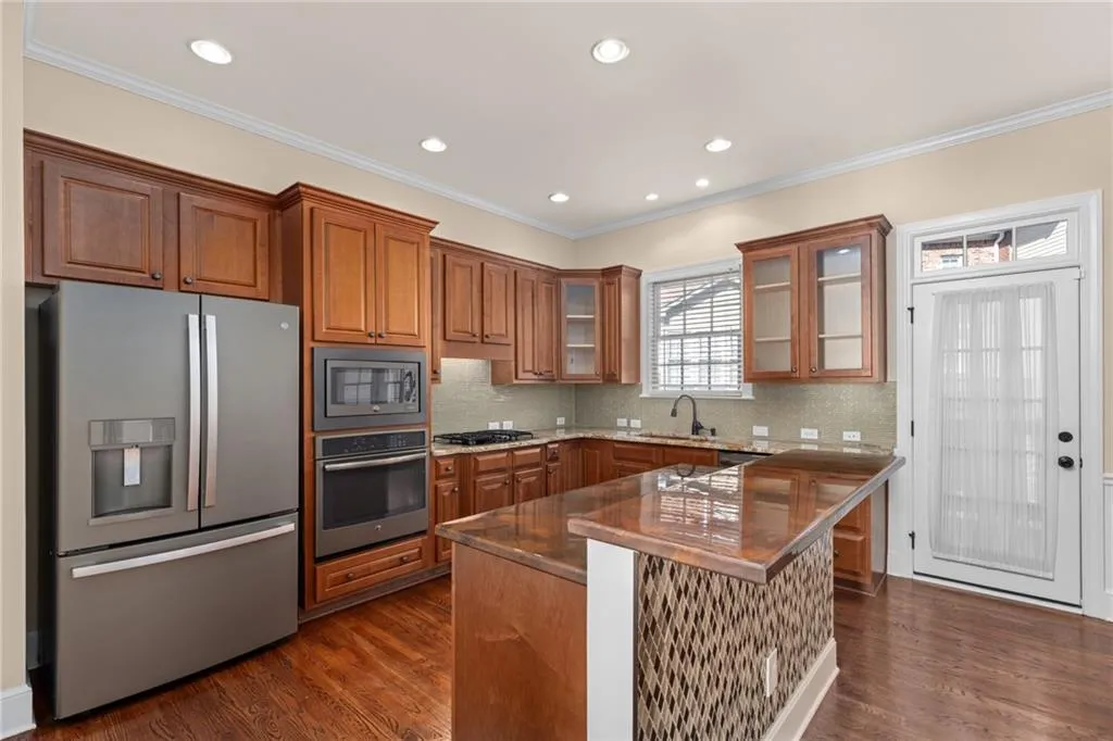 Kitchen with appliances with stainless steel finishes, dark wood-style floors, brown cabinetry, and a sink