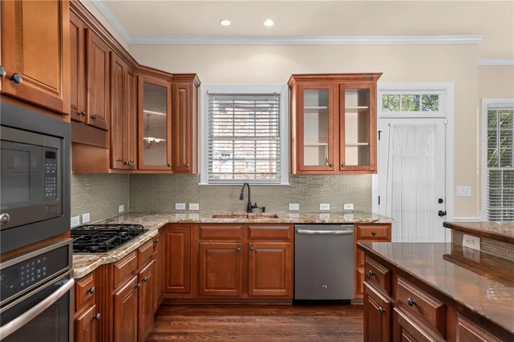 Kitchen with brown cabinetry, ornamental molding, appliances with stainless steel finishes, and a sink