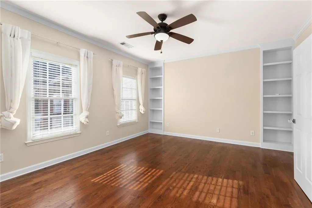 Spare room with built in shelves, ceiling fan, visible vents, baseboards, and wood finished floors