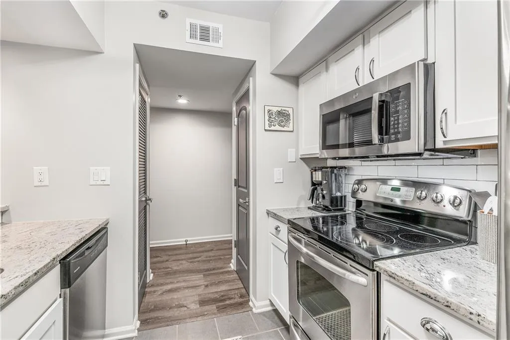 Kitchen with appliances with stainless steel finishes, white cabinetry, light stone countertops, tasteful backsplash, and light tile patterned floors