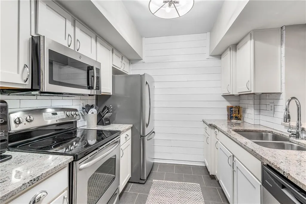 Kitchen featuring tasteful backsplash, appliances with stainless steel finishes, light stone countertops, white cabinets, and wooden walls