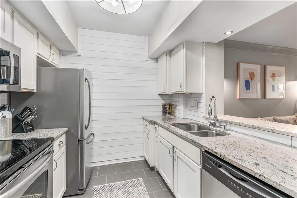 Kitchen with light stone counters, white cabinetry, stainless steel appliances, backsplash, and crown molding