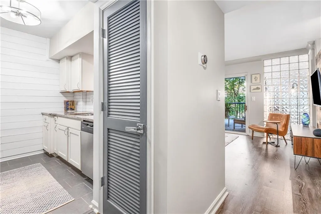 Kitchen with white cabinetry, backsplash, light stone counters, dishwasher, and wooden walls