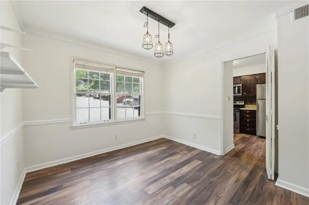 Unfurnished dining area with dark wood-type flooring, crown molding, and a chandelier