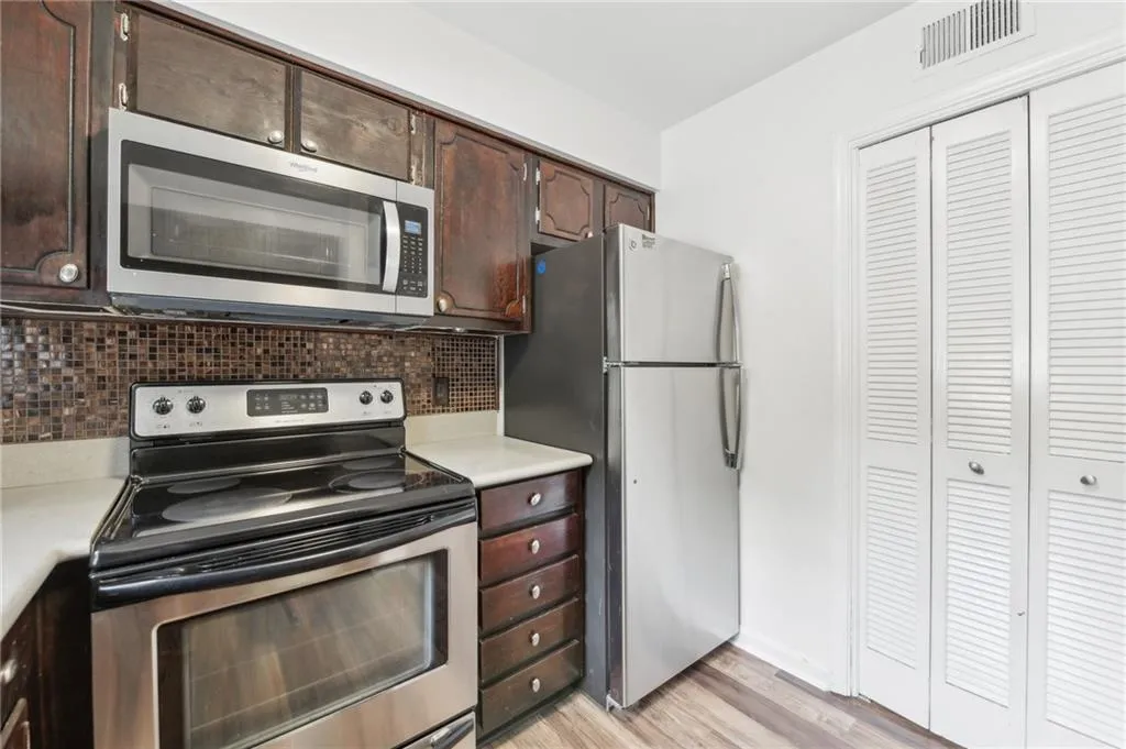 Kitchen with stainless steel appliances, light countertops, decorative backsplash, and dark brown cabinetry
