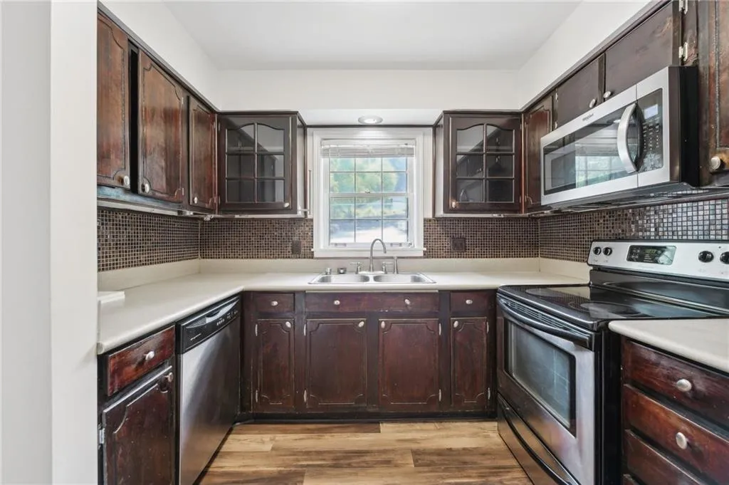 Kitchen with stainless steel appliances, decorative backsplash, light countertops, light wood-style flooring, and dark brown cabinets