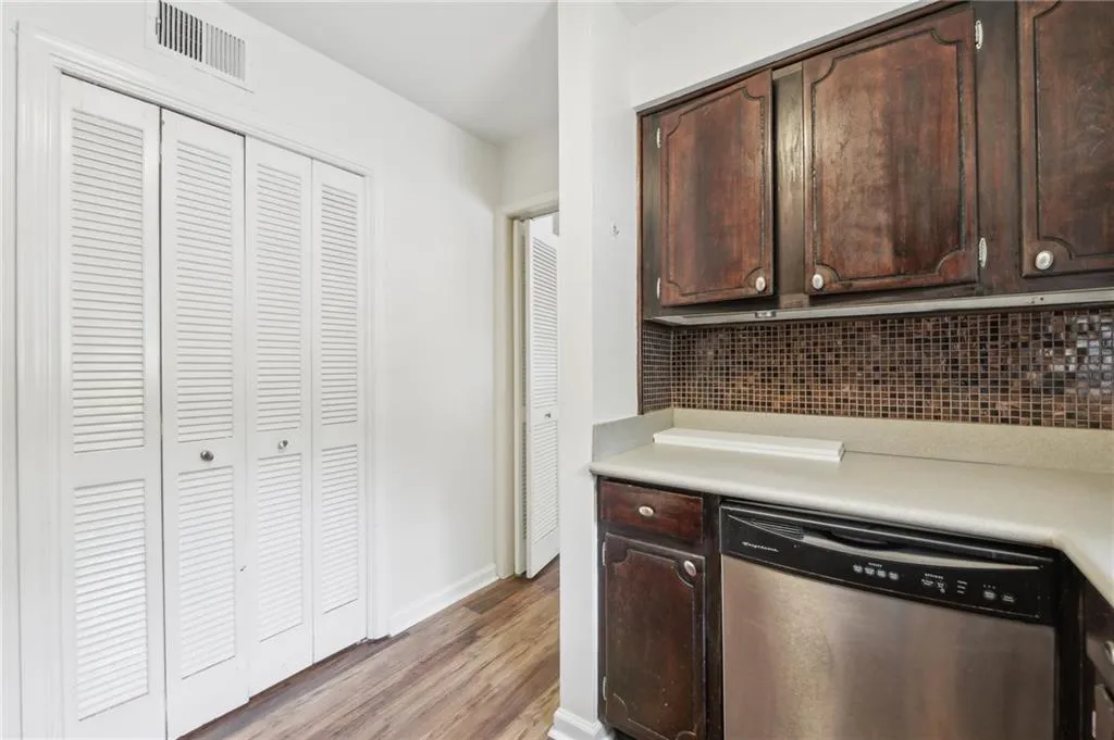 Kitchen with stainless steel dishwasher, light wood-style flooring, dark brown cabinetry, decorative backsplash, and light countertops