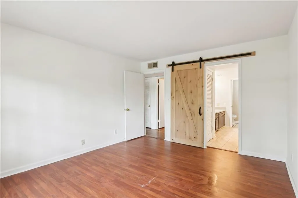 Unfurnished bedroom featuring a barn door, wood finished floors, and ensuite bath