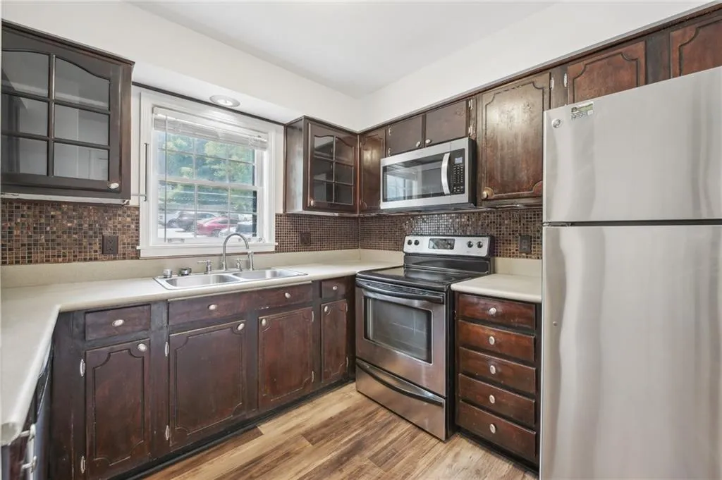 Kitchen with stainless steel appliances, dark brown cabinetry, light wood-style floors, decorative backsplash, and glass insert cabinets