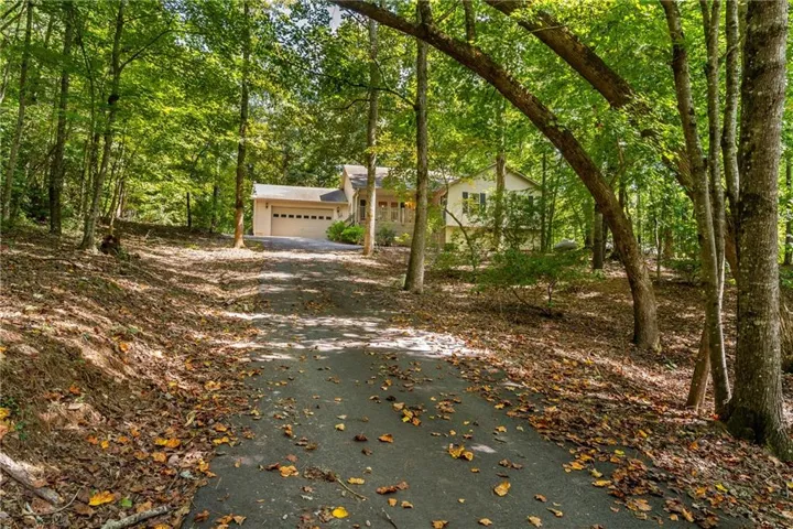 Paved driveway leading to a residence with a two-car garage, surrounded by mature trees