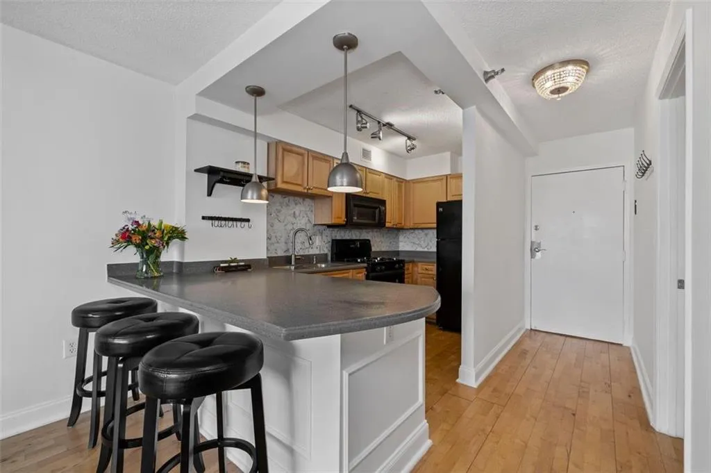 Kitchen featuring dark countertops, tasteful backsplash, light wood-type flooring, a peninsula, and black appliances