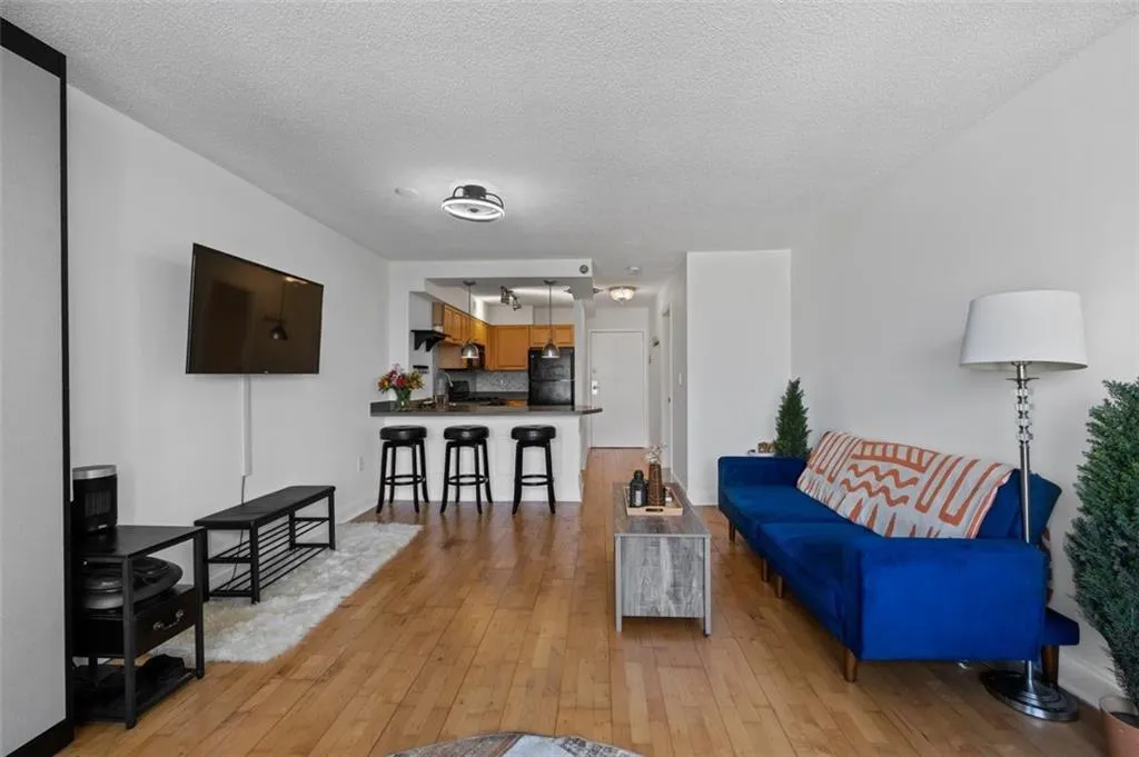 Living room with a textured ceiling, light wood-type flooring, and baseboards