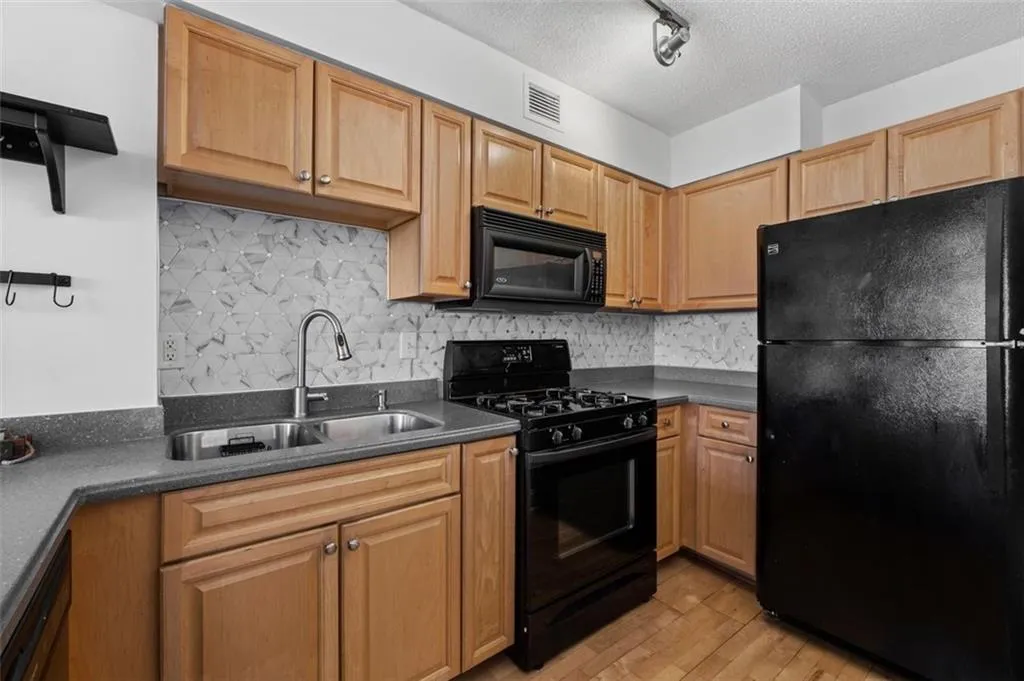 Kitchen with visible vents, a sink, black appliances, dark countertops, and light wood-type flooring