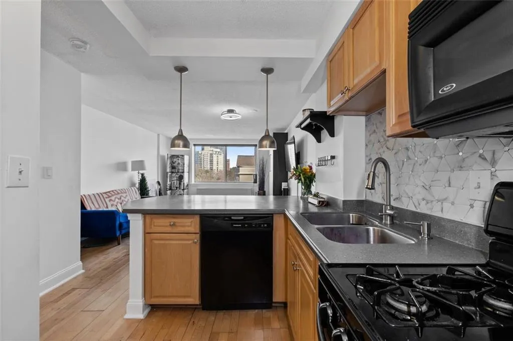 Kitchen with a peninsula, light wood-style flooring, a sink, black appliances, and dark countertops