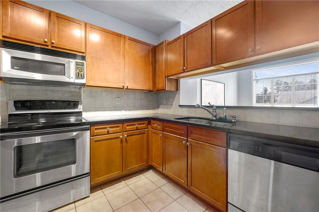 Kitchen with appliances with stainless steel finishes, brown cabinets, light tile patterned floors, tasteful backsplash, and a textured ceiling